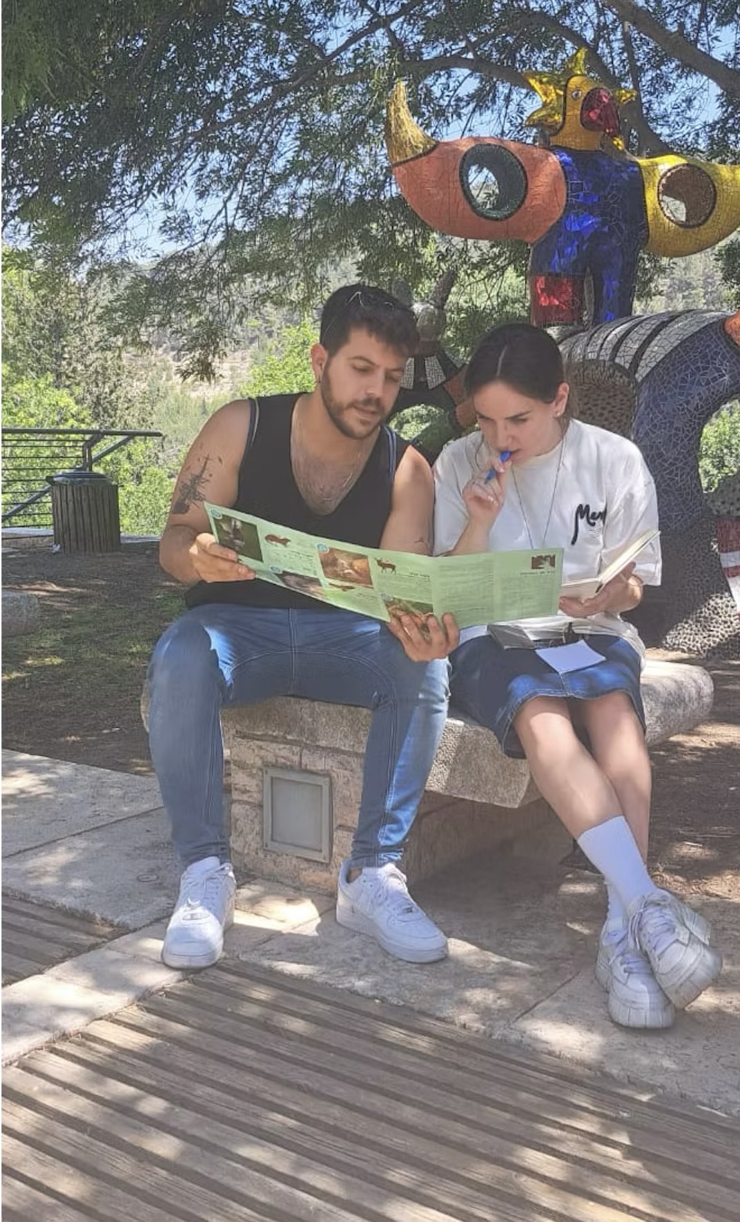 שני אנשים יושבים על ספסל בגן ומעיינים בעלון מודפס